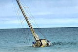 An old yacht sits on the sea bed in water barely a metre deep.