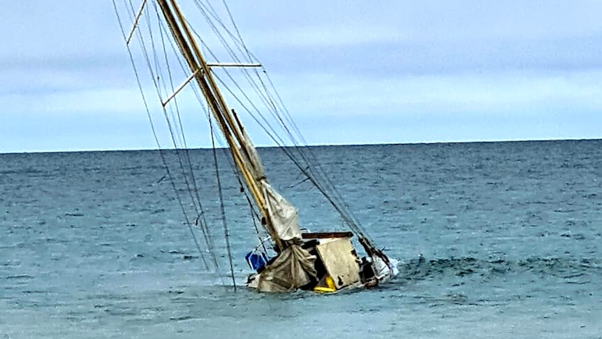 An old yacht sits on the sea bed in water barely a metre deep.