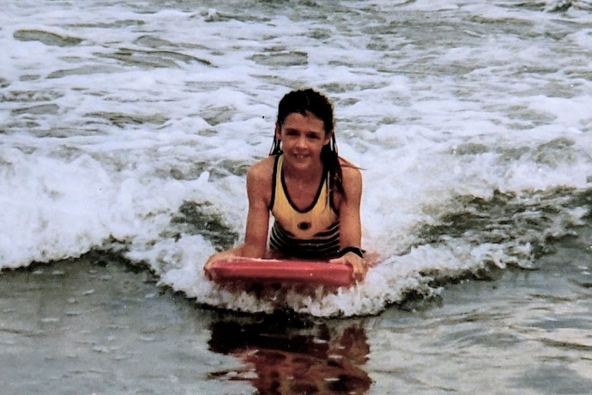 Sophie Vivian rides a wave in on a board while lying on her stomach.