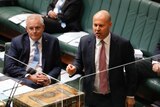 Josh Frydenberg speaks in parliament behind a clear glass screen. Scott Morrison is seated to his right, listening.