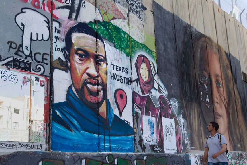 A man walks past and looks at a painting of George Floyd on a wall in the West Bank.