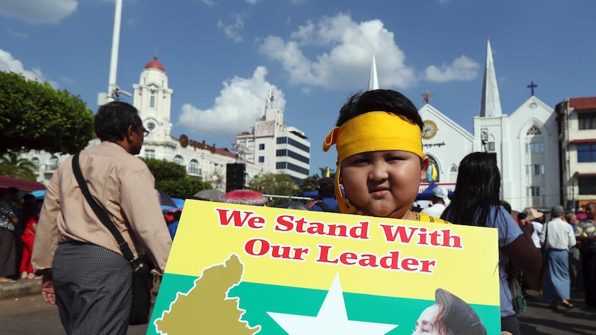 A boy with Karen ethnic attire holds placard with picture of Myanmar leader Aung San Suu Kyi.