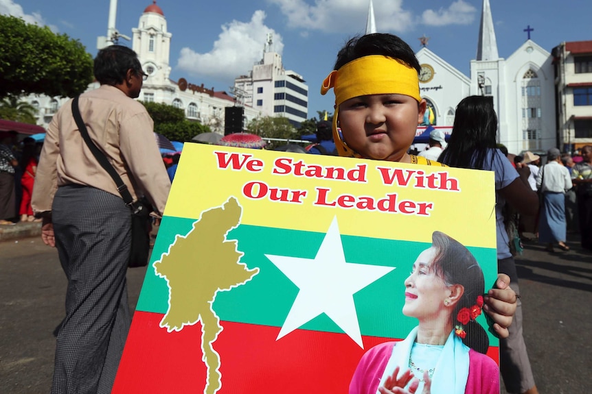 A young boy holds a poster reading 'we stand with our leader'