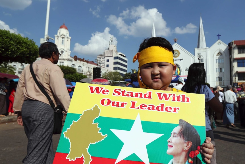 A boy with Karen ethnic attire holds placard with picture of Myanmar leader Aung San Suu Kyi.