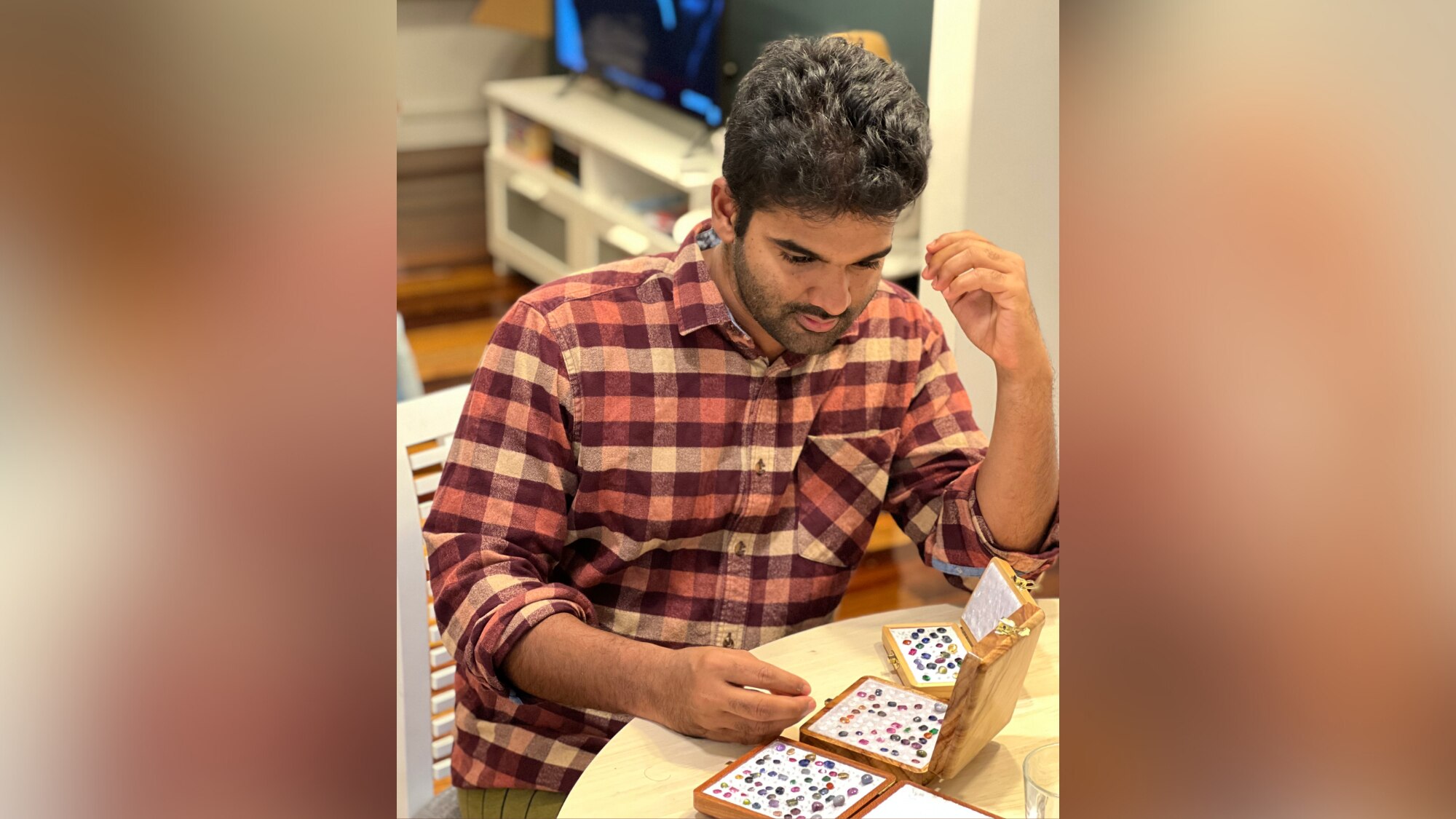 A photo of Anfas Azad inspecting precious stones. He is wearing a checkered shirt. He has black hair, a close-shaved beard. 