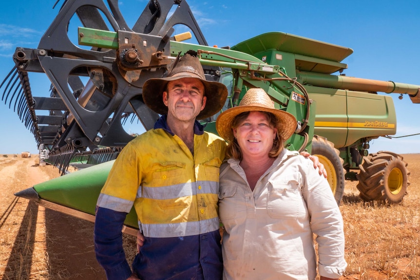 A man and a woman stand in front of their wheat harvester