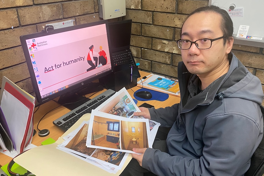 Man at computer looking at printed paper photos in his hand