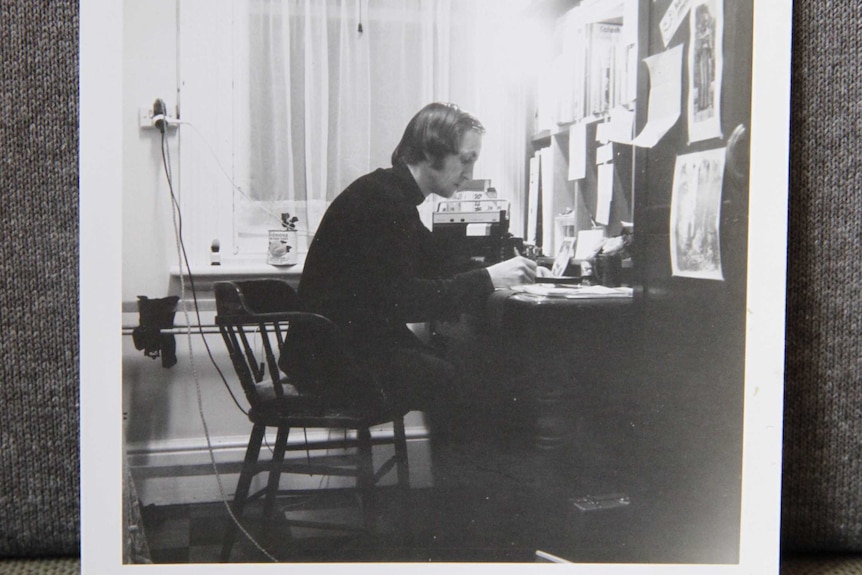 A black-and-white photo of a man sitting at a desk, writing on paper.