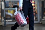 A man walks on the street holding a plastic bag, which contains a bag of ice.