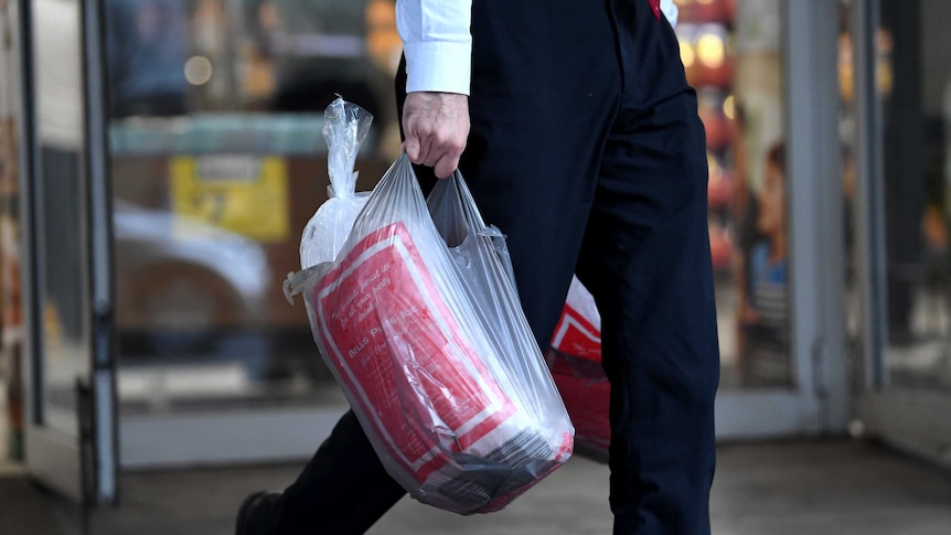 A man walks on the street holding a plastic bag, which contains a bag of ice.