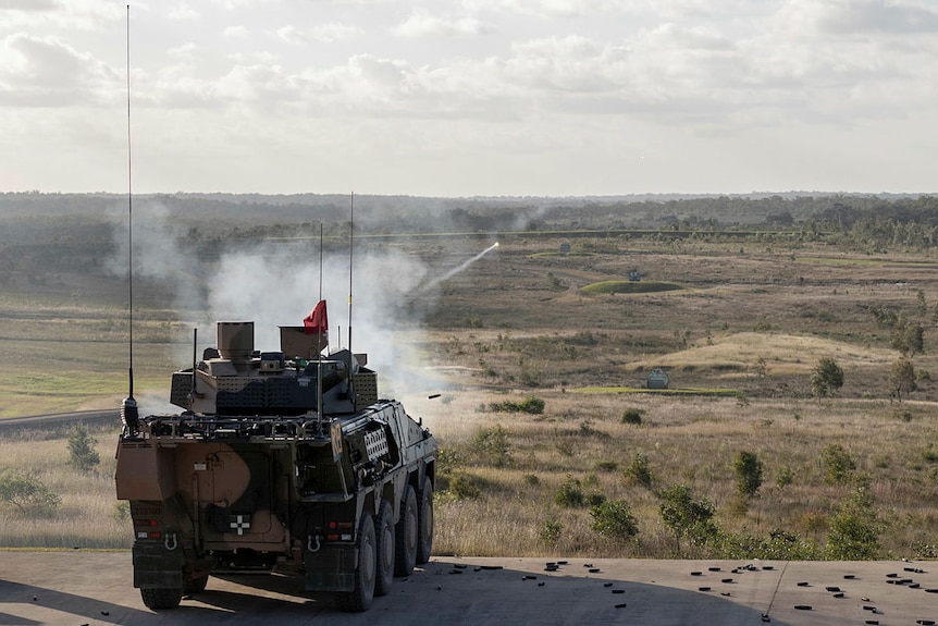 A military vehicle similar to a tank fires a shot out across the horizon, with smoke rising from the cannon.