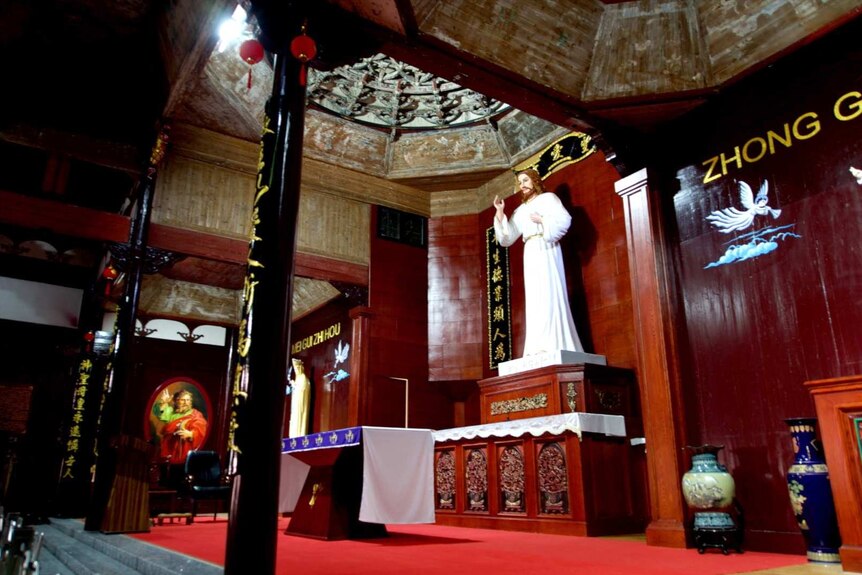 A large statue of Jesus stands inside a building with red carpet and Chinese calligraphy on the walls and pillars