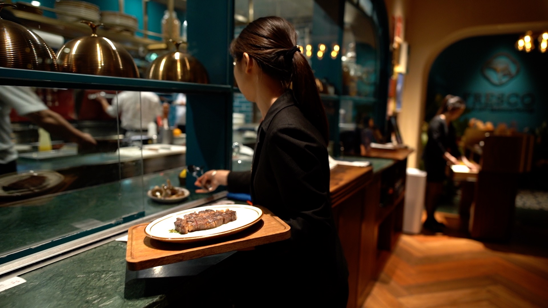 Un camarero sostiene una bandeja de madera con un plato y un filete.