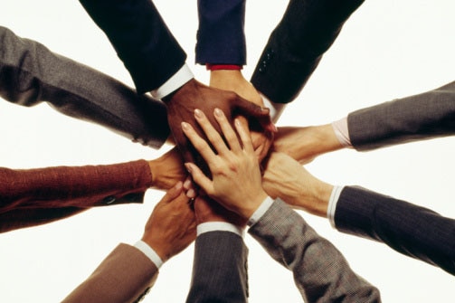 A collection of hands with different skin colours resting on top of one another.