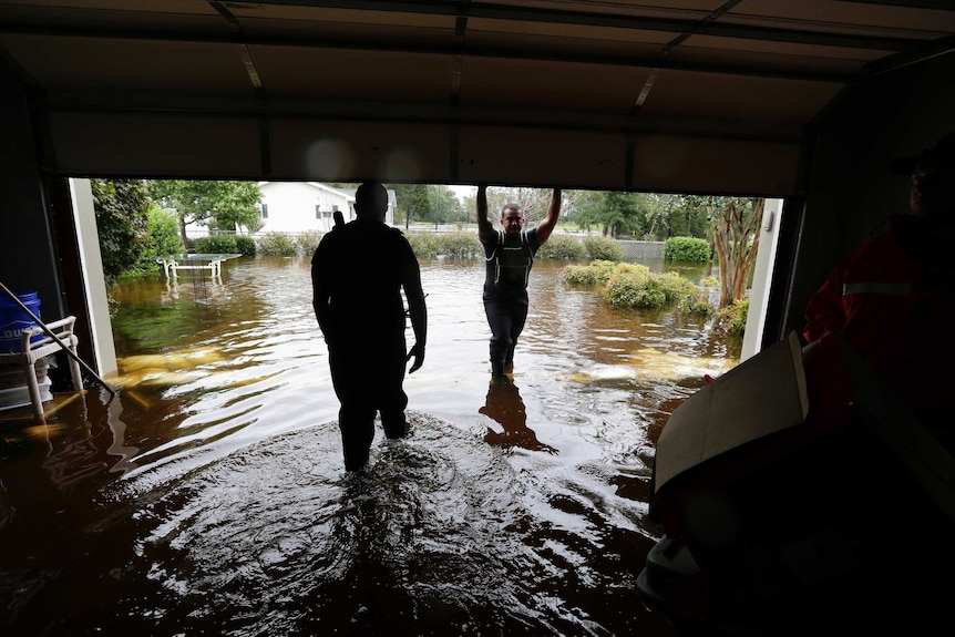 A photo taken from inside a garage shows two figures wading through calf-deep floodwaters