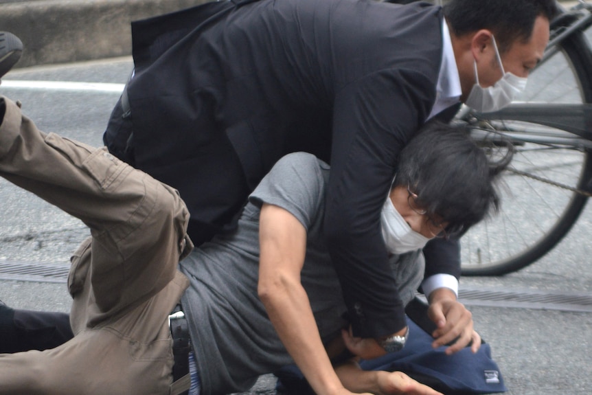 a man wearing a face mask and glasses is held on to the road by a man in a suit and face mask