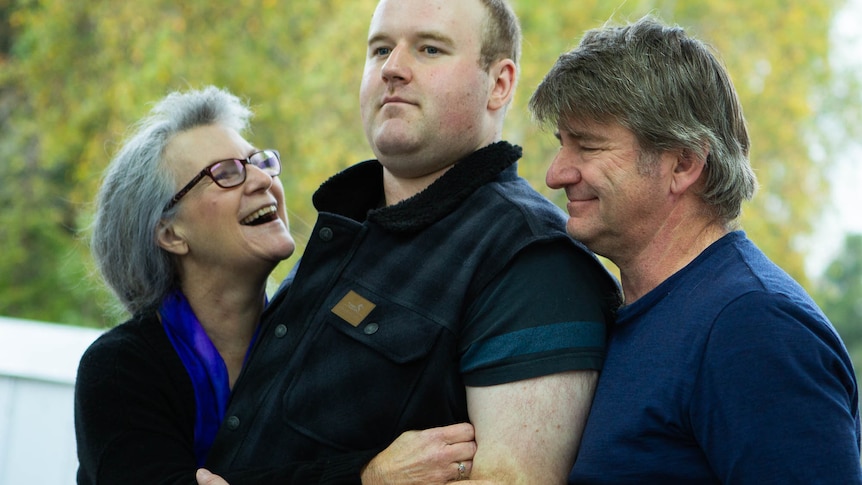 Smiling parents cuddle up to their very large 25 year old son.