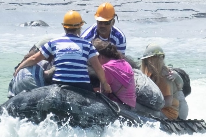 A small black dingy carried a group of survivors away from an ash-covered island.