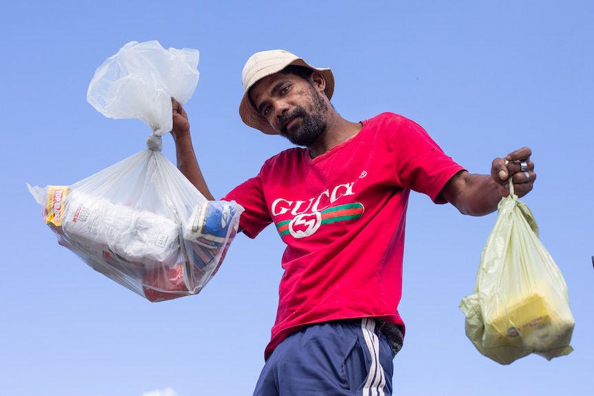 Man in red t-ishirt and white bucket hat holding a food parcel in each hand