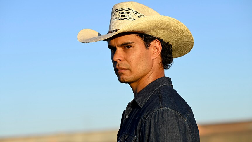 A young man wearing a cowboy-style hat in the Australian outback.
