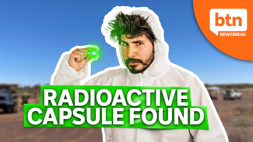 Joe dressed in one piece protective hazmat suit holds up a radioactive pill.
