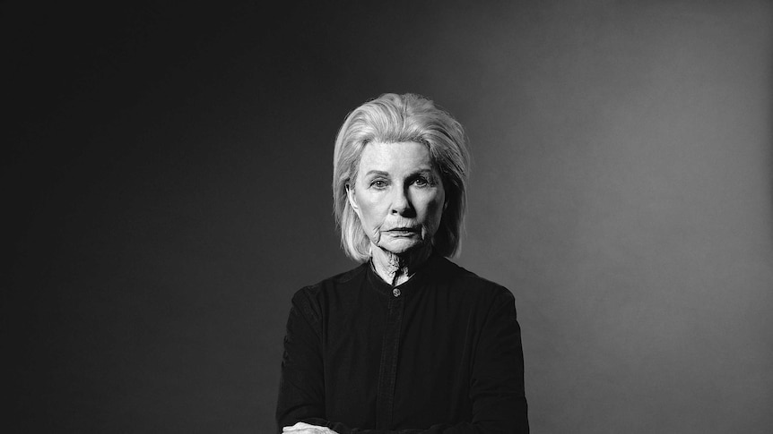 A black and white image of Robyn Nevin looking at the camera in a bare black space.