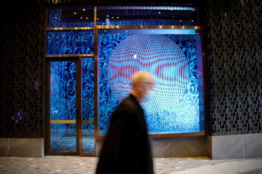 A pedestrian wearing a face mask walks past a light-filled art installation.