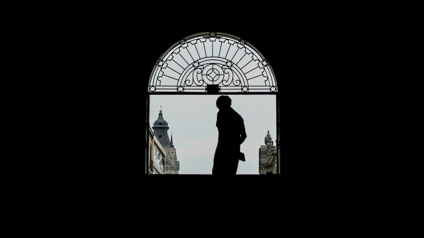 The silhouette of a person standing in an arched church window, looking outwards.