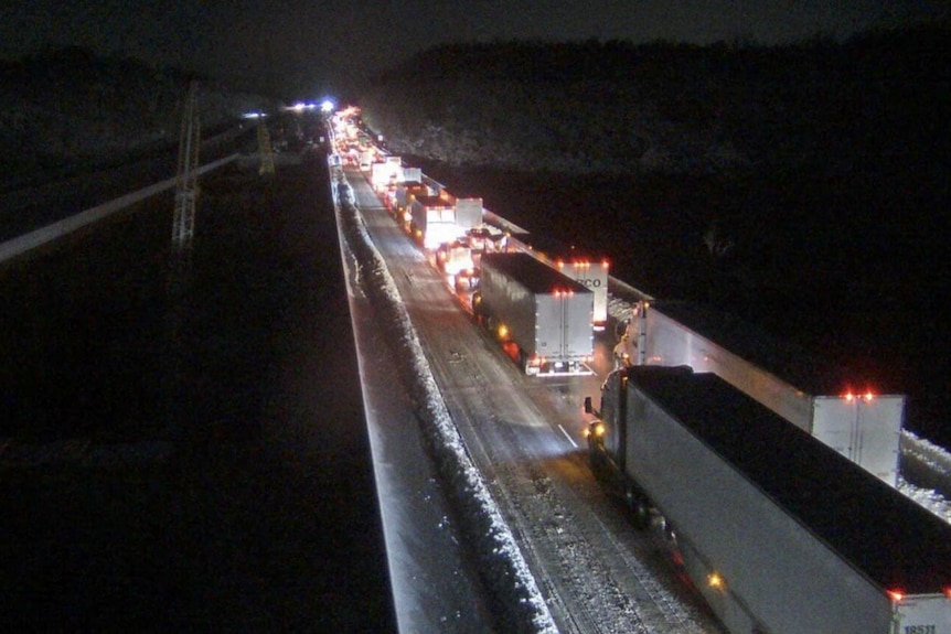 Lights from a line of trucks light up an icy highway during a cold night 