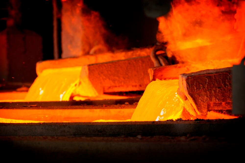 Bright orange liquid copper pours from a pipe as steam rises off it.