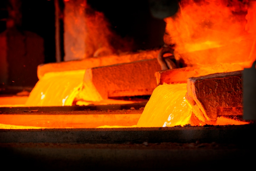 Bright orange liquid copper pours from a pipe as steam rises off it.