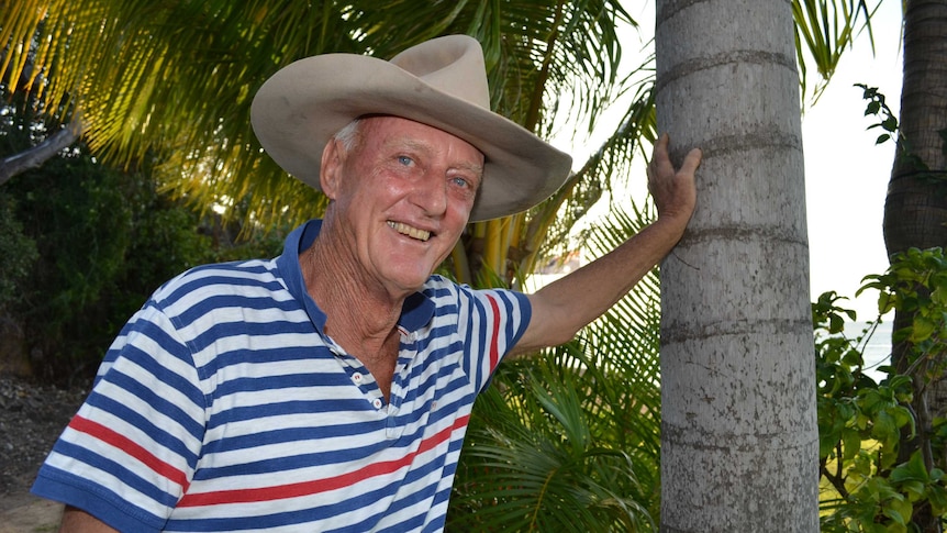 A man wearing a big hat, standing under a palm tree
