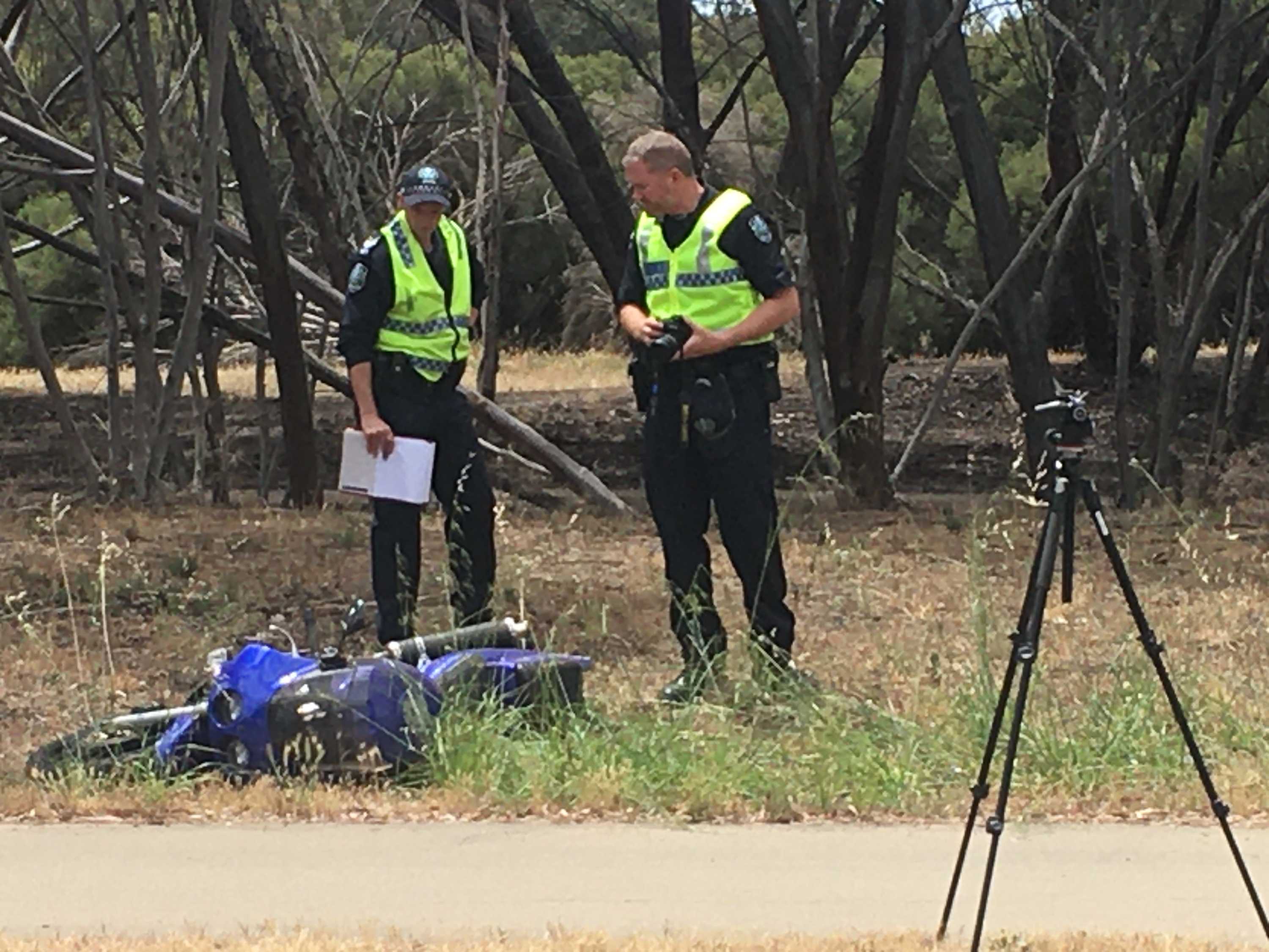 Two police officers look at a motorcycle involved in a crash on the side of a road