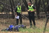 Two police officers look at a motorcycle involved in a crash on the side of a road