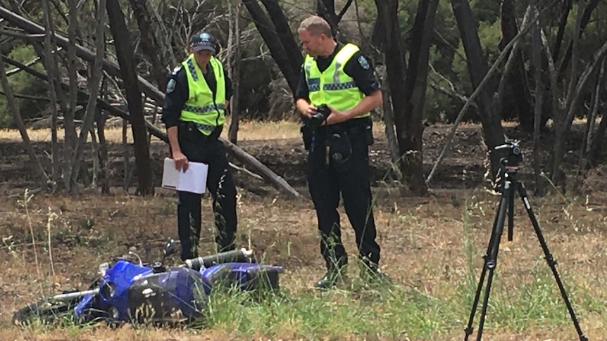 Two police officers look at a motorcycle involved in a crash on the side of a road