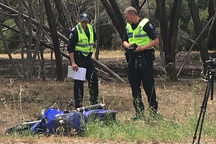 Two police officers look at a motorcycle involved in a crash on the side of a road