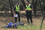 Two police officers look at a motorcycle involved in a crash on the side of a road