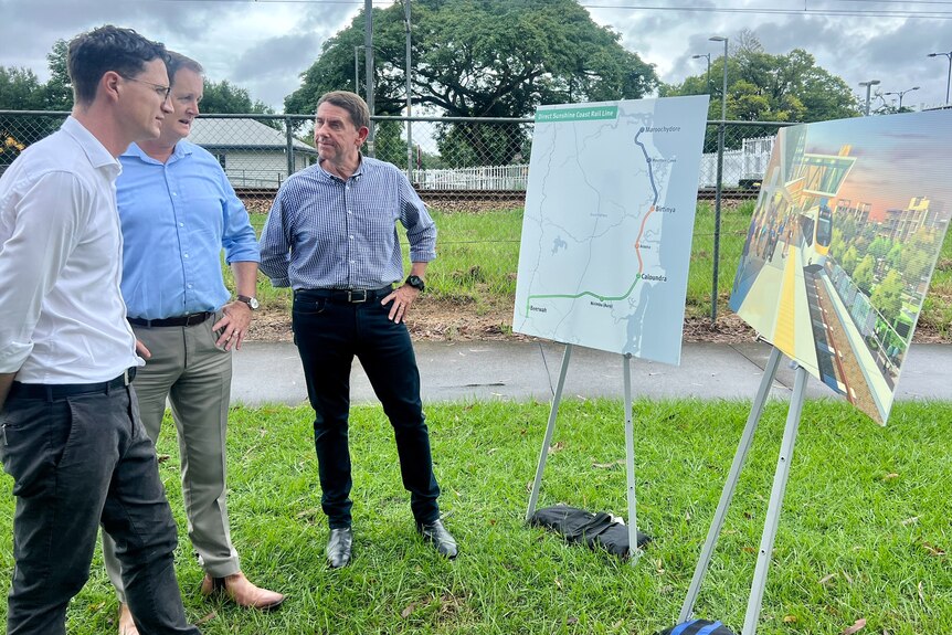 Tres políticos varones miran un mapa de la nueva línea ferroviaria de Sunshine Coast.