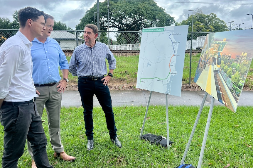 Tres políticos varones miran un mapa de la nueva línea ferroviaria de Sunshine Coast.