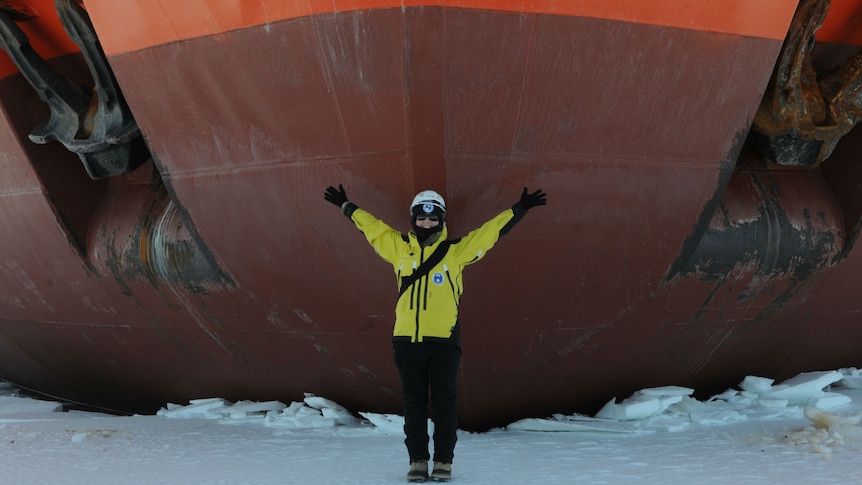 A woman stands in front of the Aurora Australis ship with her arms out