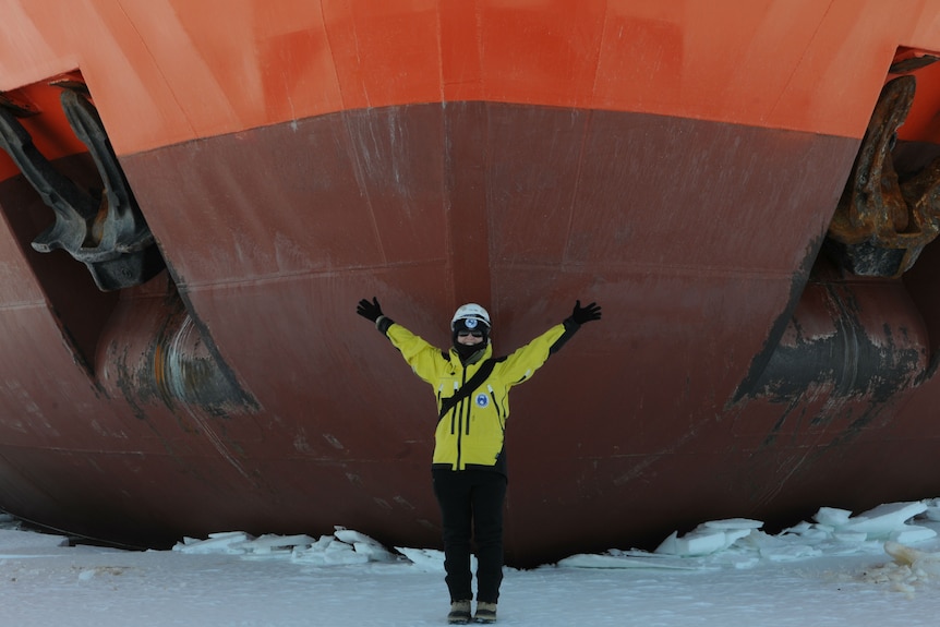 A woman stands in front of the Aurora Australis ship with her arms out