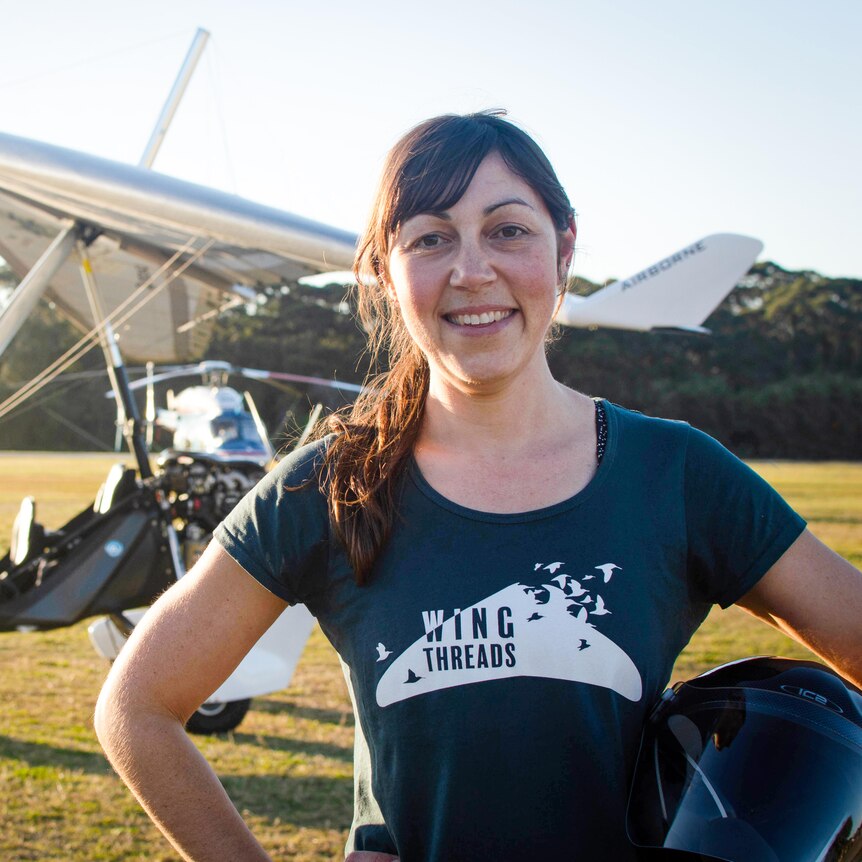 A woman smiling at the camera with a small plane in the background