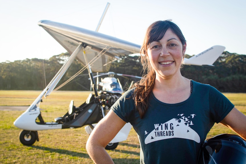 A woman smiling at the camera with a small plane in the background