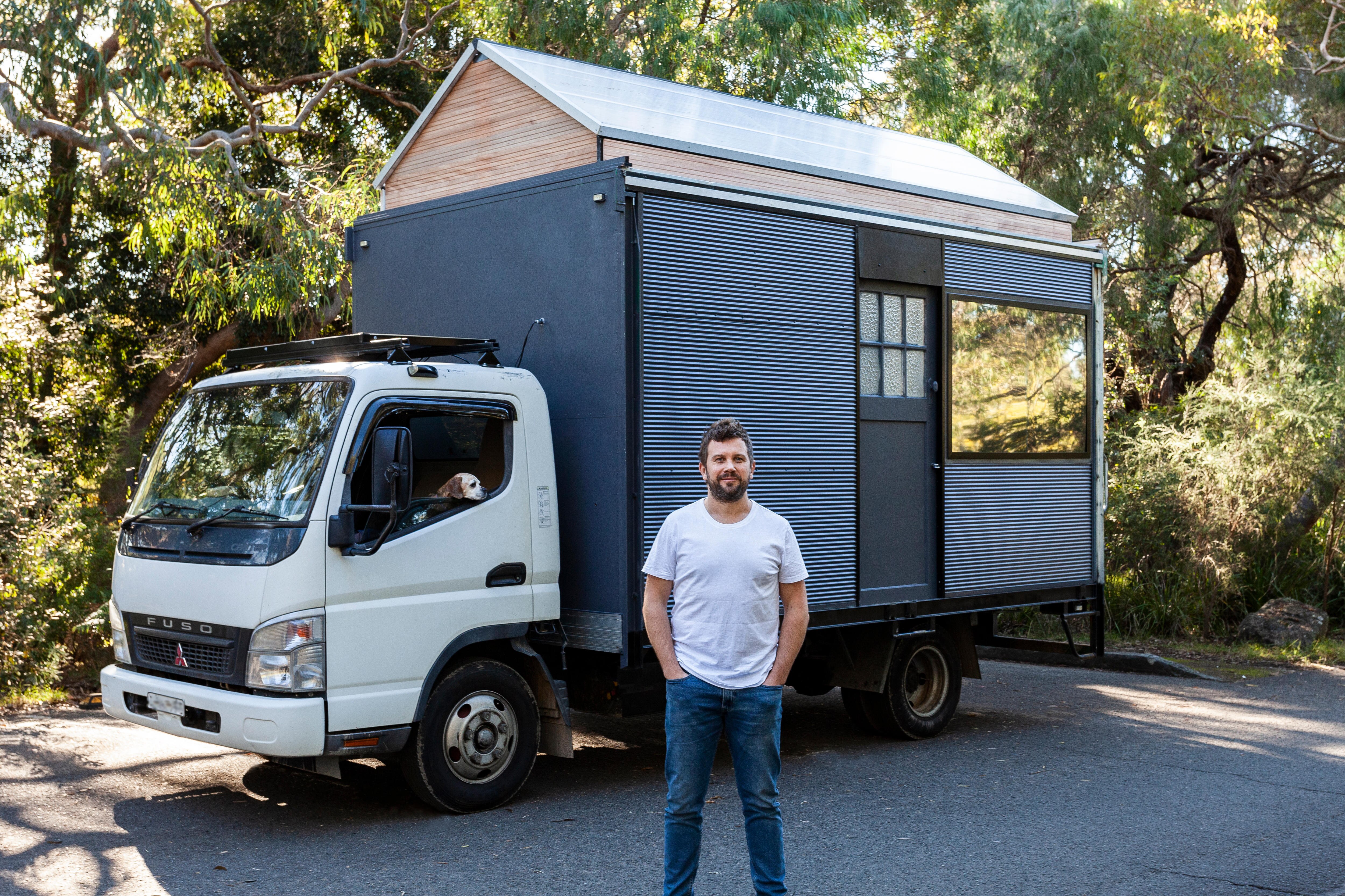 A man stands in front of a truck with a tiny home on the back.