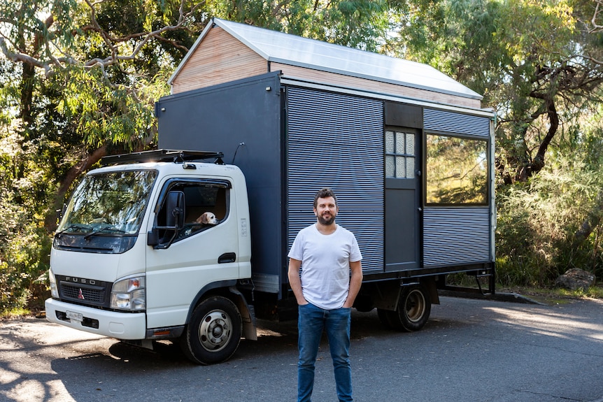 A man stands in front of a truck with a tiny home on the back.