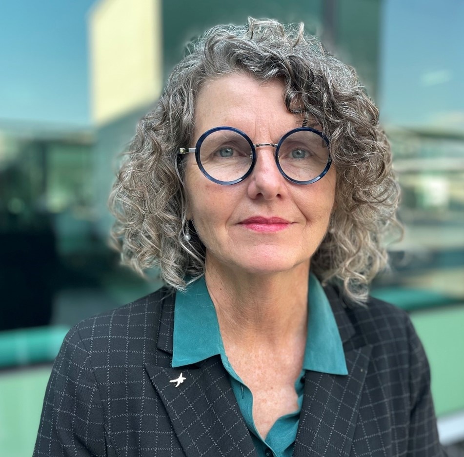 Foto de cabeza de Christina Pollard. Tiene el pelo rizado y gafas azules redondas.