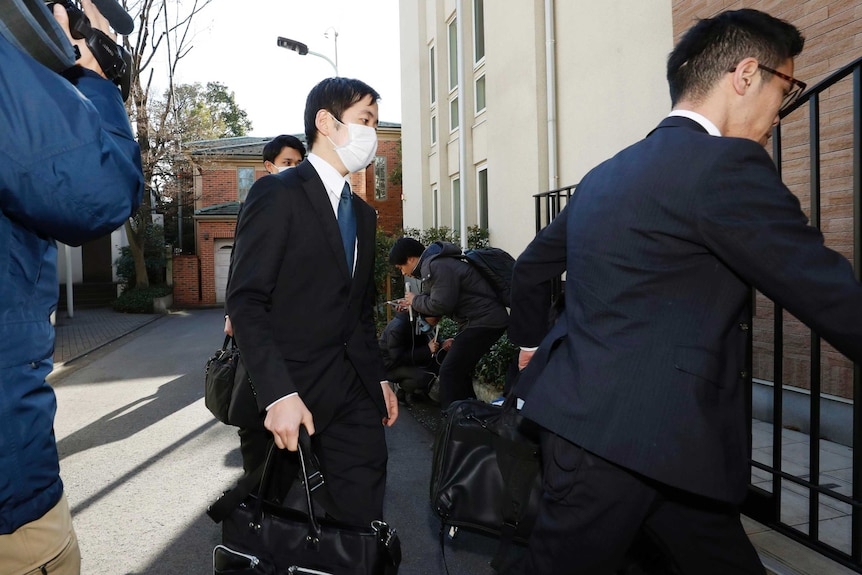 men in face masks and suits arrive in front of television cameras outside a house in Tokyo