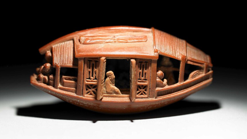 An intricately carved sculpture of people aboard a Chinese boat.