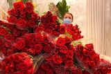 A woman is standing behind hundreds of red roses