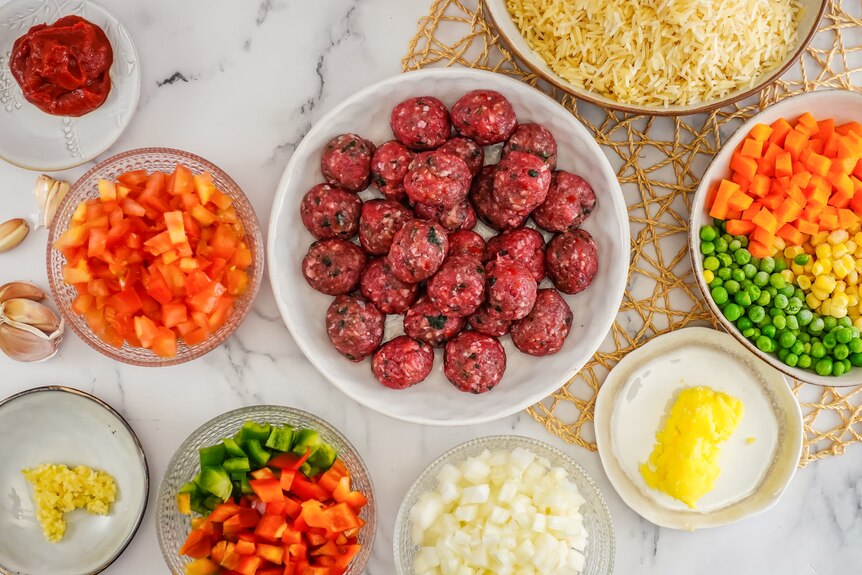 Aerial shot of ingredients on a bench including raw meatballs in a bowl, diced vegetables and ghee on a plate